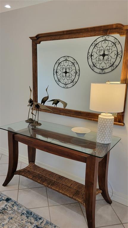 A glass-topped console table with a woven shelf sits beneath a large wooden-framed mirror — 7557 FAIRLINKS COURT, SARASOTA, FL