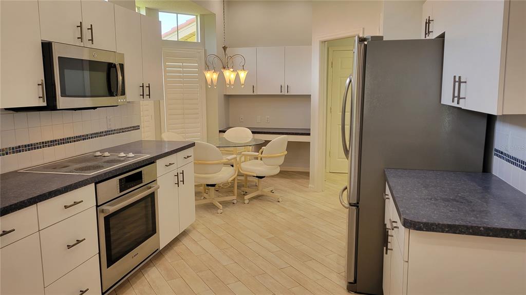 A kitchen with white cabinets, dark countertops, stainless steel appliances, and a small dining area — 7557 FAIRLINKS COURT, SARASOTA, FL