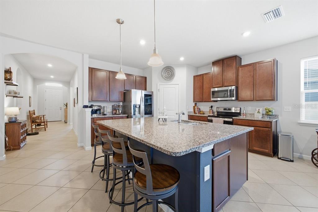 A kitchen features a large granite-topped island, dark wood cabinets, and tile flooring — 5907 114TH AVENUE E, PARRISH, FL