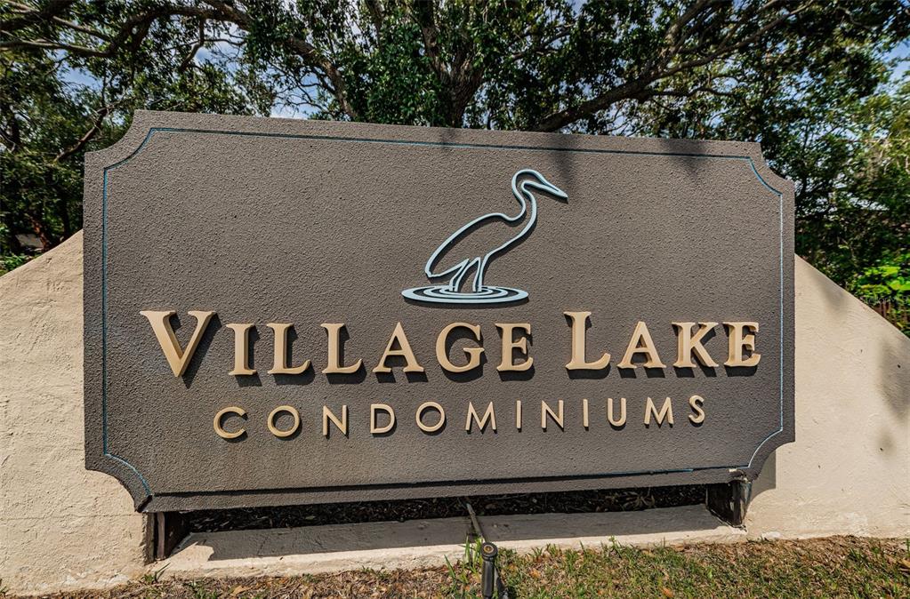 A sign for Village Lake Condominiums features a heron icon against a dark textured background — 781 VILLAGE LAKE TERRACE N UNIT 101A, ST PETERSBURG, FL