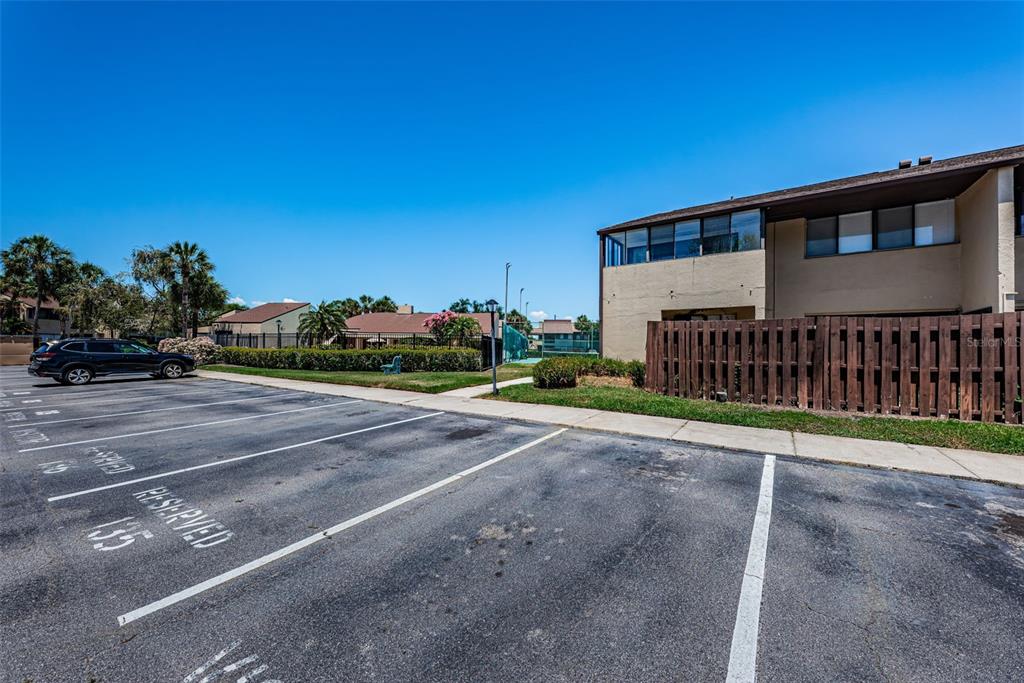 An outdoor parking lot sits in front of a multi-story building with a wooden fence — 781 VILLAGE LAKE TERRACE N UNIT 101A, ST PETERSBURG, FL