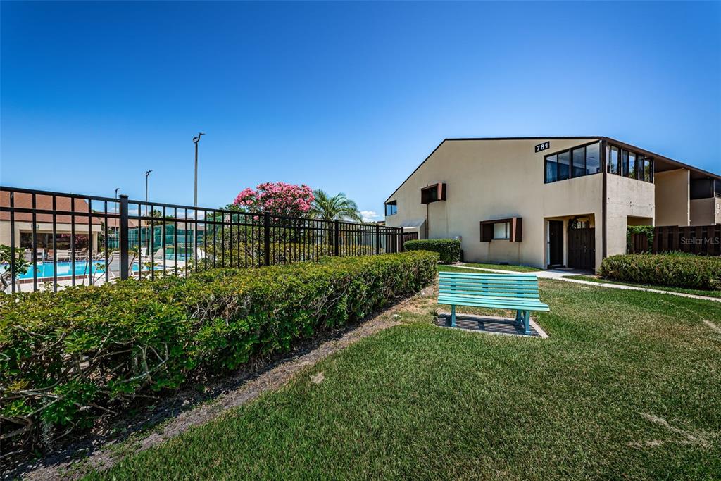 A light blue bench sits on a grassy lawn next to a two-story building — 781 VILLAGE LAKE TERRACE N UNIT 101A, ST PETERSBURG, FL