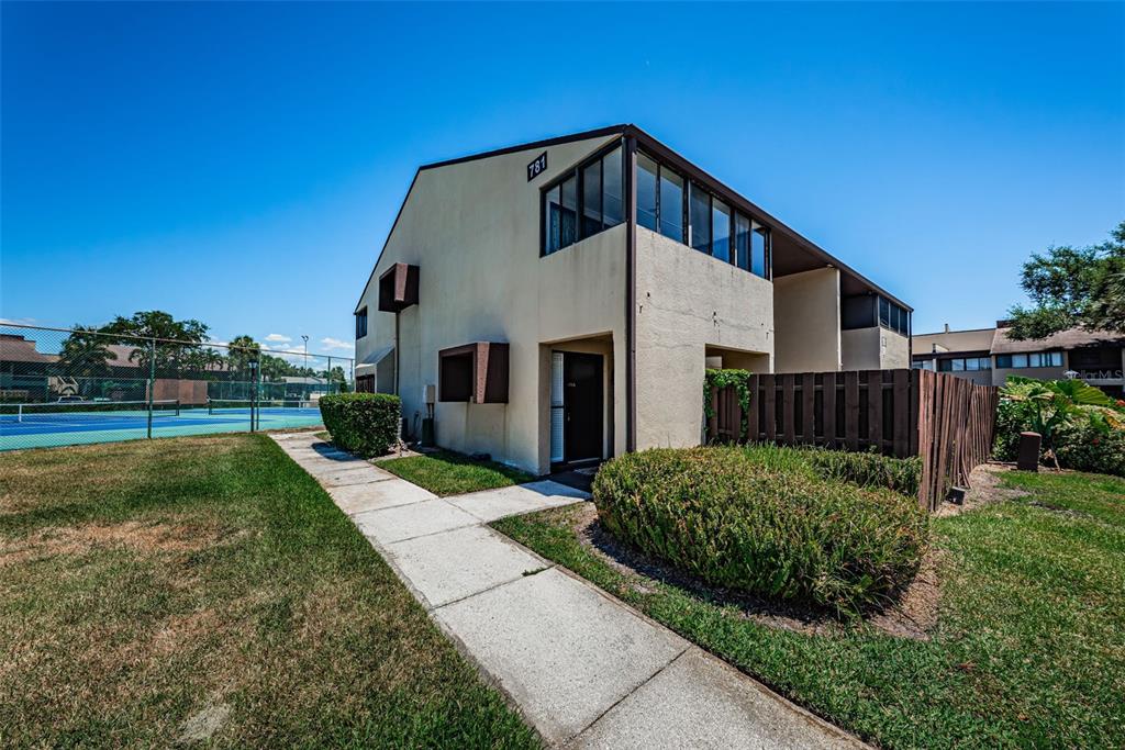 Exterior view of a two-story residential building with a tennis court and sidewalk nearby — 781 VILLAGE LAKE TERRACE N UNIT 101A, ST PETERSBURG, FL