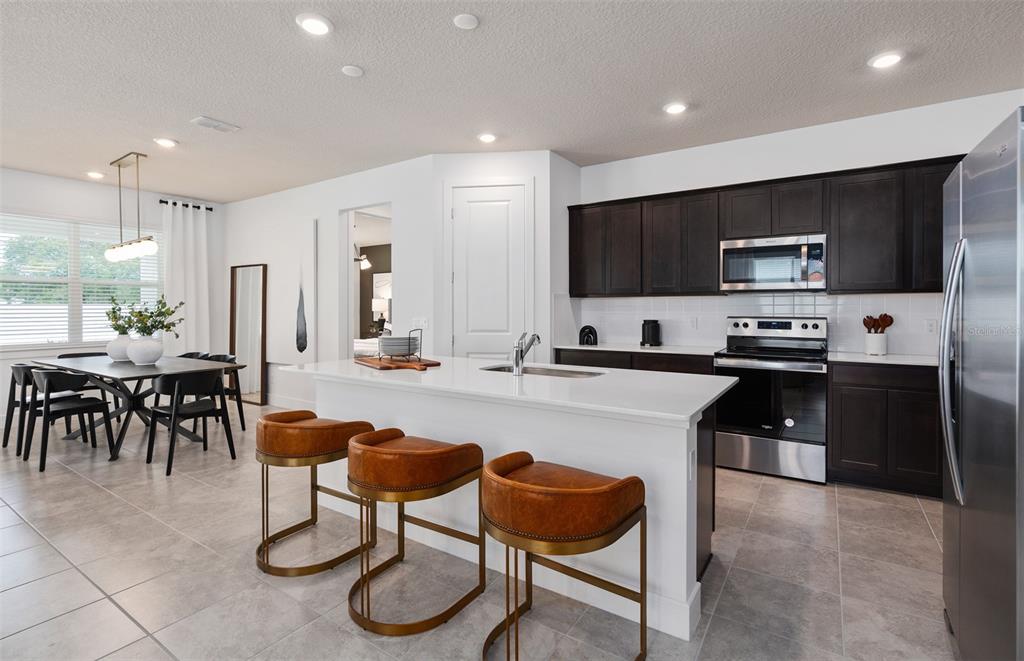A modern kitchen features dark wood cabinets, a white island with bar stools, and tile flooring — 4747 HARRINGTON FIELDS DRIVE, DAVENPORT, FL