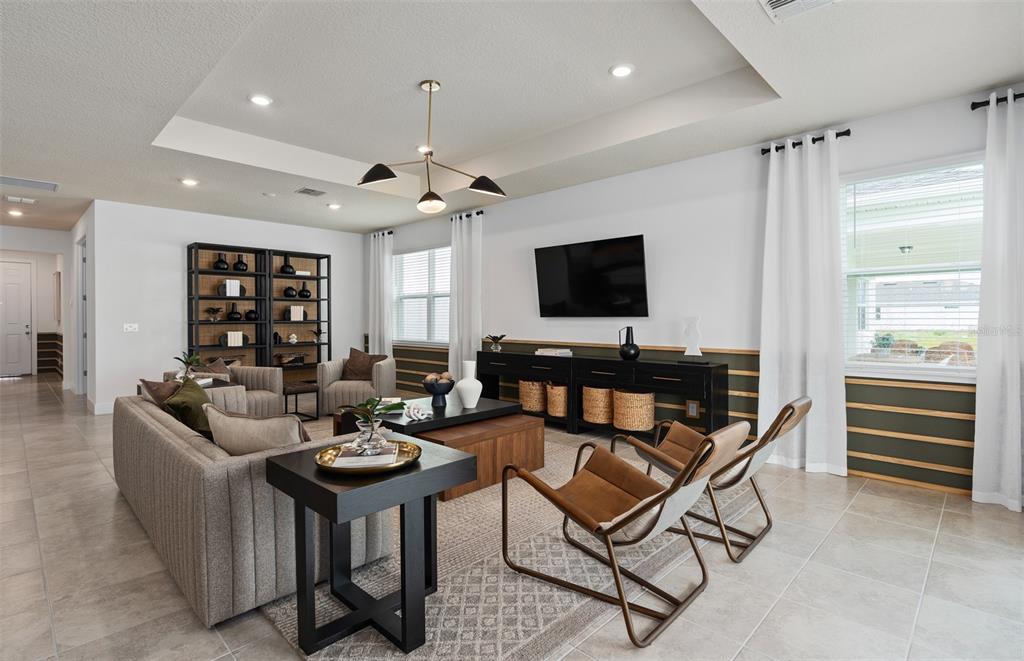 A living room features a tray ceiling, a wall-mounted television, and modern furniture — 4747 HARRINGTON FIELDS DRIVE, DAVENPORT, FL
