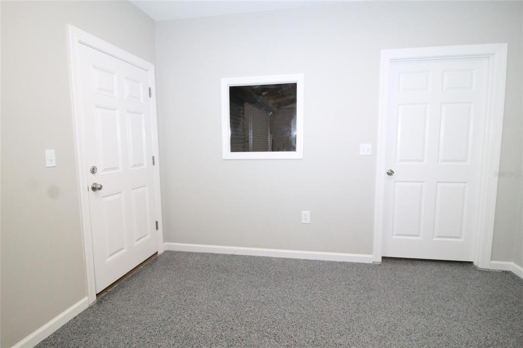 A room with gray carpet, two white doors, and a square window looking into a garage — 114 W MYERS BOULEVARD, MASCOTTE, FL