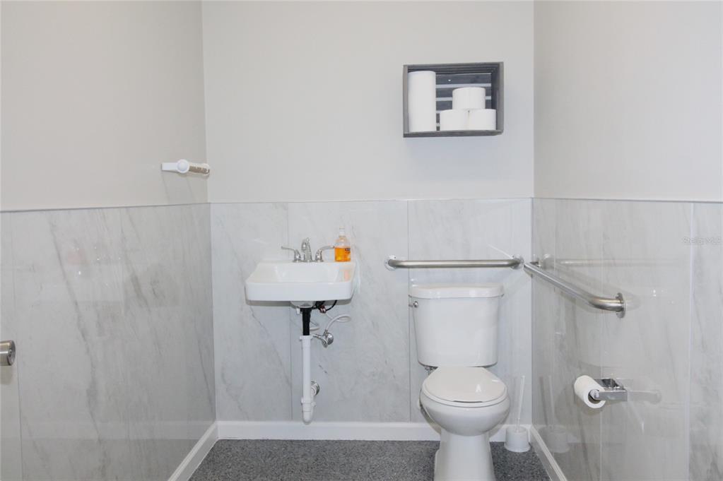 A small bathroom features a wall-mounted sink, a toilet with grab bars, and marble-look tile — 114 W MYERS BOULEVARD, MASCOTTE, FL