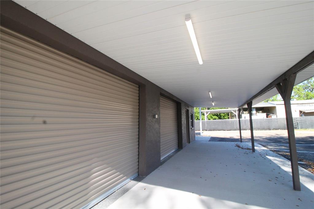 A covered concrete walkway leads to two roll-up garage doors under a white ceiling — 114 W MYERS BOULEVARD, MASCOTTE, FL