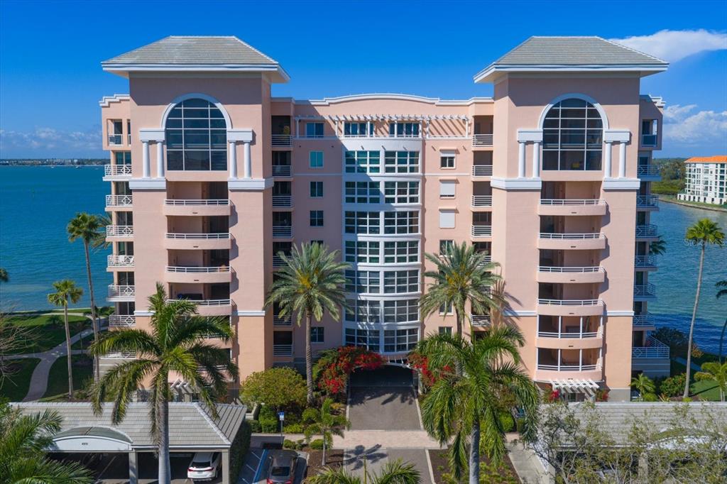 An exterior view of a multi-story peach-colored condominium building with palm trees and water — 4993 BACOPA LANE S UNIT 505, ST PETERSBURG, FL