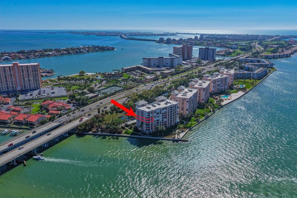 An aerial view shows a multi-story waterfront condominium building next to a bridge and road — 4993 BACOPA LANE S UNIT 505, ST PETERSBURG, FL