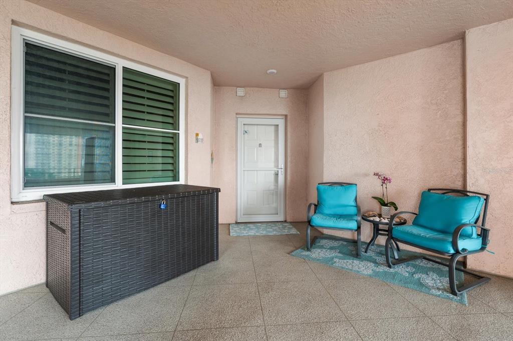 A covered balcony features a storage chest, two chairs with blue cushions, and a door — 4993 BACOPA LANE S UNIT 505, ST PETERSBURG, FL