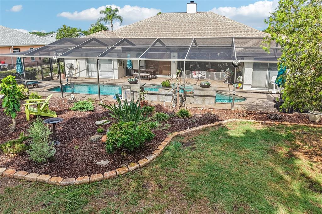 A backyard features a screened-in swimming pool, a patio, and a landscaped garden bed — 213 N BROCKFIELD DRIVE, SUN CITY CENTER, FL