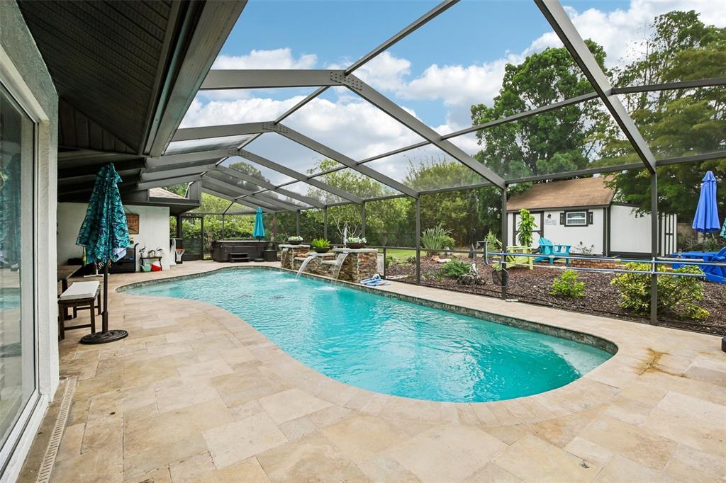 A screened-in patio features a swimming pool with water features and stone tile decking — 213 N BROCKFIELD DRIVE, SUN CITY CENTER, FL