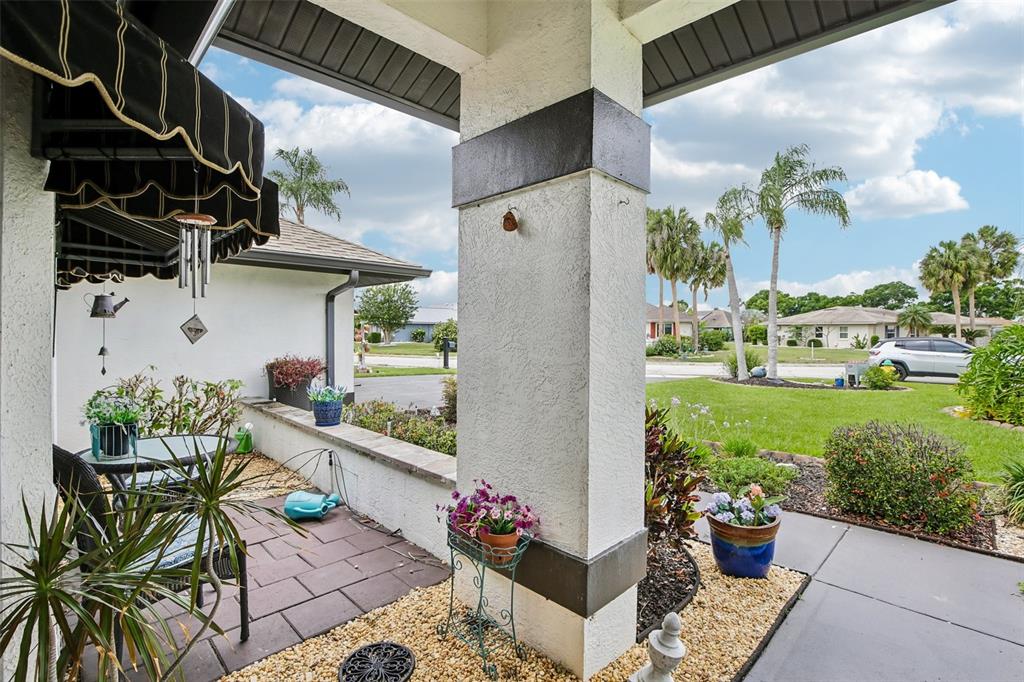 A covered patio features a tiled floor, a stucco pillar, and potted plants — 213 N BROCKFIELD DRIVE, SUN CITY CENTER, FL