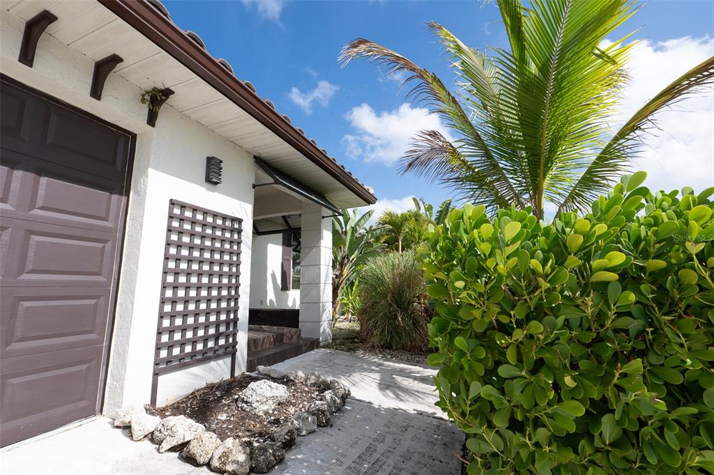 A white house exterior features a brown garage door, a trellis, and lush tropical landscaping — 376 PORTOFINO DRIVE, PUNTA GORDA, FL