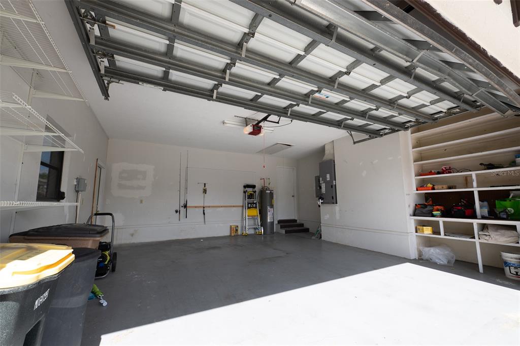 A garage with a concrete floor, open overhead door, storage shelving, and a water heater — 376 PORTOFINO DRIVE, PUNTA GORDA, FL