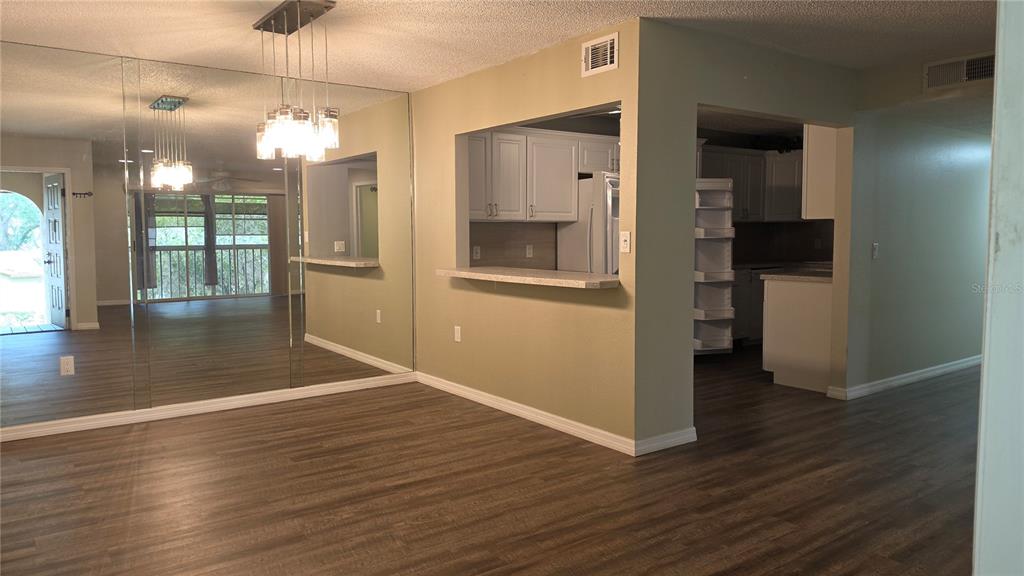 A living area with wood-look flooring, a mirrored wall, and a kitchen pass-through window — 12119 SUNNY GLEN LANE UNIT E2, HUDSON, FL