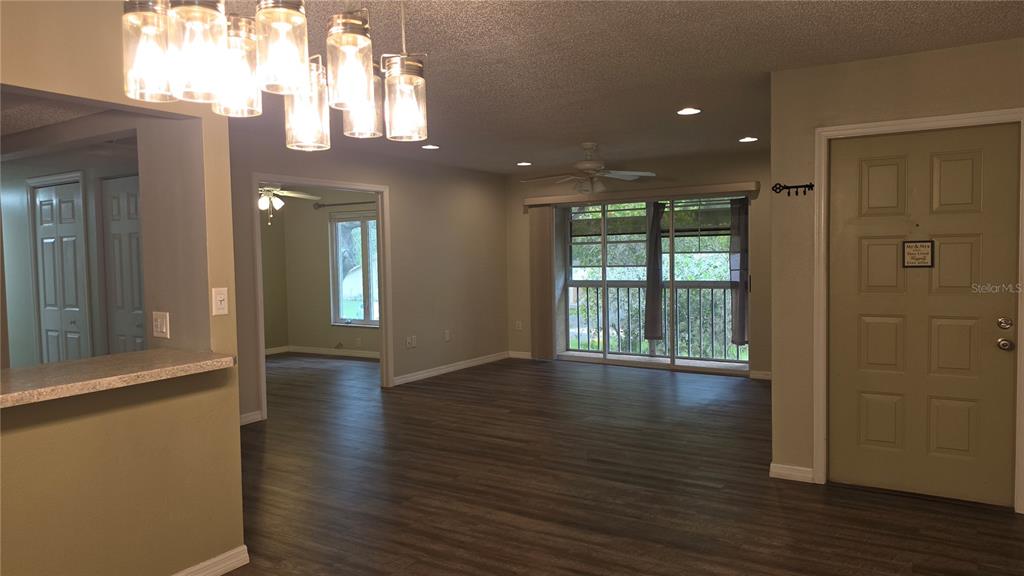 An open-concept living area features wood-look flooring, a modern chandelier, and a sliding glass door — 12119 SUNNY GLEN LANE UNIT E2, HUDSON, FL