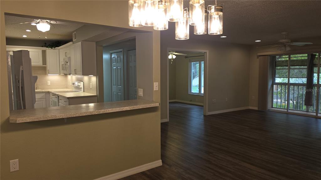 A kitchen with white cabinets and a breakfast bar overlooks a living area with flooring — 12119 SUNNY GLEN LANE UNIT E2, HUDSON, FL
