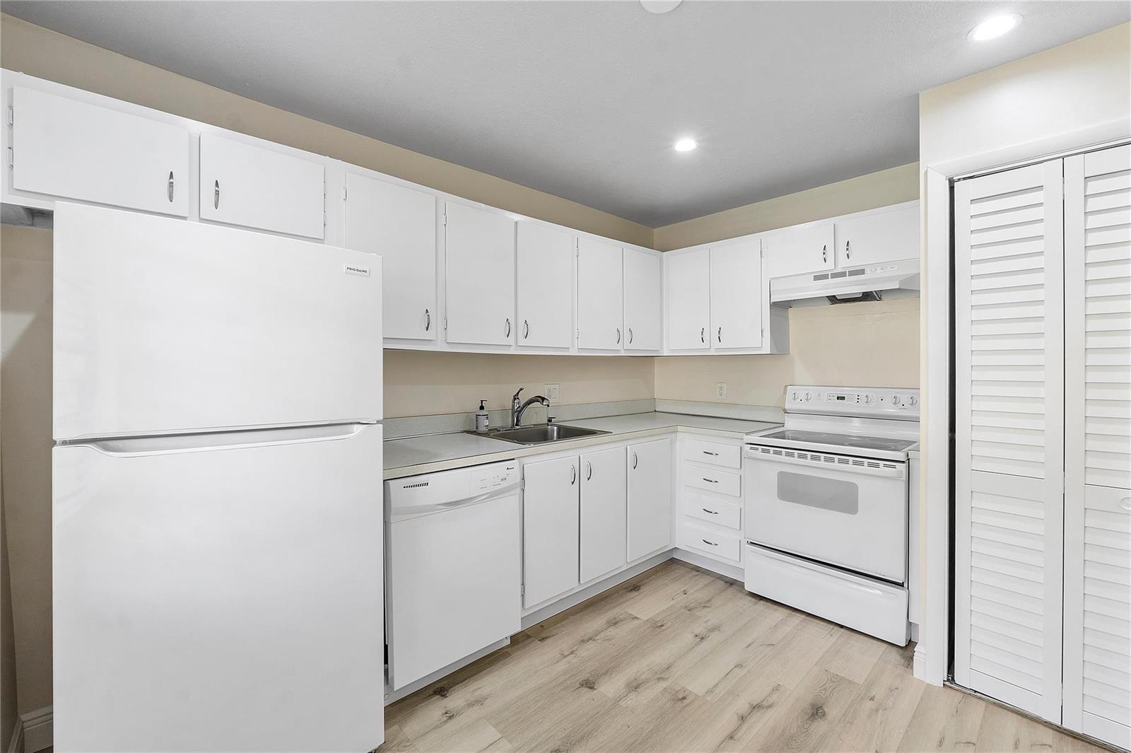 A kitchen features white cabinets, white appliances, a stainless steel sink, and light wood flooring — 21542 Juego Circle # 27h, Boca Raton FL 33433, BOCA RATON, FL