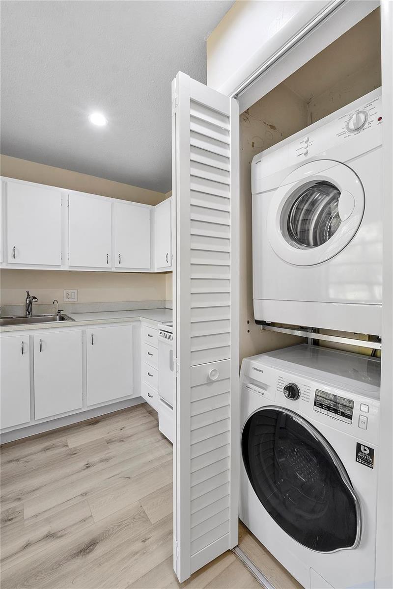 A laundry closet with a stacked washer and dryer sits beside a kitchen with white cabinets — 21542 Juego Circle # 27h, Boca Raton FL 33433, BOCA RATON, FL