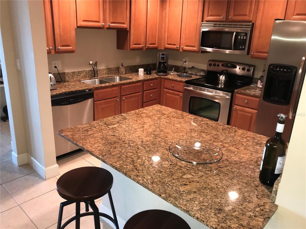 A kitchen features wood cabinets, granite countertops, stainless steel appliances, and a breakfast bar — 808 3RD AVENUE W UNIT 509, BRADENTON, FL