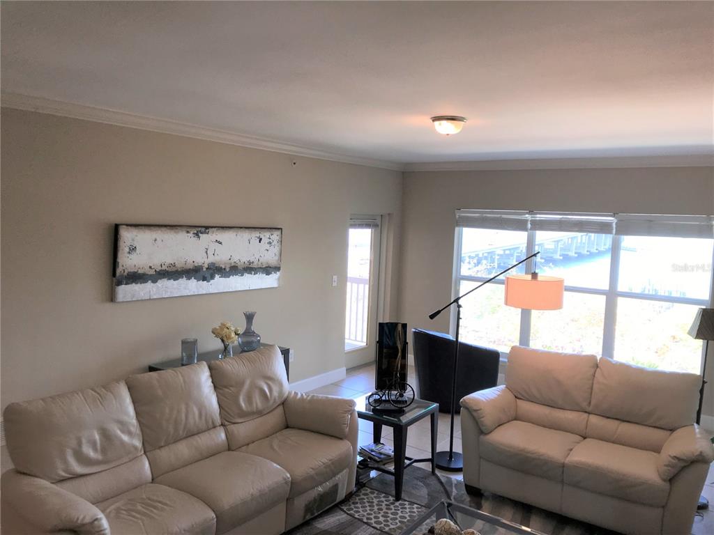 A living room features two beige leather sofas, a glass-topped side table, and large windows — 808 3RD AVENUE W UNIT 509, BRADENTON, FL