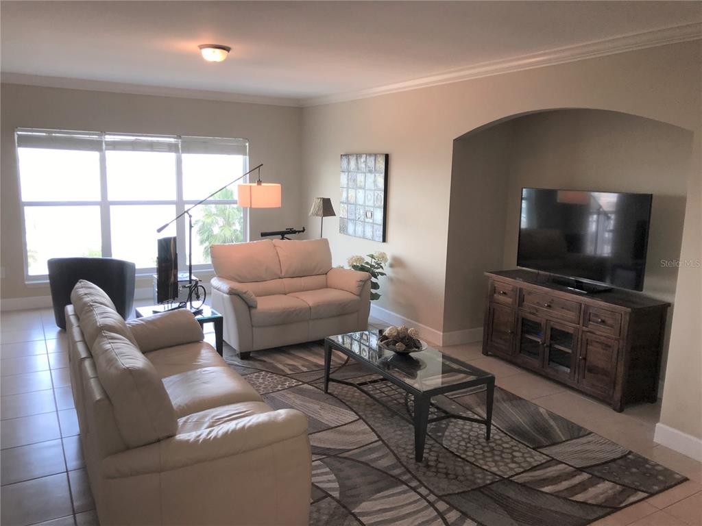 A living room features a white sofa and loveseat, a glass coffee table, and a television — 808 3RD AVENUE W UNIT 509, BRADENTON, FL