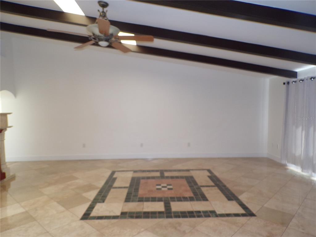 A living room features a vaulted ceiling with dark wood beams and tiled flooring — 179 MARIA COURT, PUNTA GORDA, FL