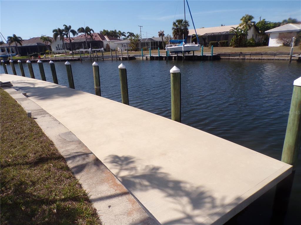 A concrete dock extends along a canal lined with wooden pilings and residential homes — 179 MARIA COURT, PUNTA GORDA, FL