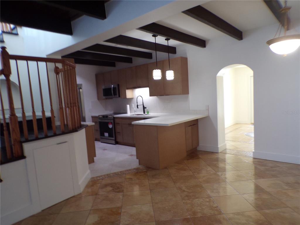 A kitchen with wood cabinets, white countertops, and dark ceiling beams overlooks a tiled floor — 179 MARIA COURT, PUNTA GORDA, FL