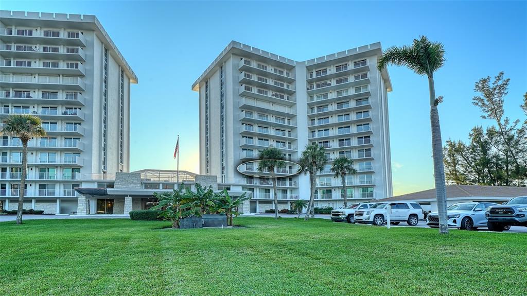 A multi-story apartment building with balconies stands behind a lawn and a parking area — 2301 GULF OF MEXICO DRIVE UNIT 44N, LONGBOAT KEY, FL