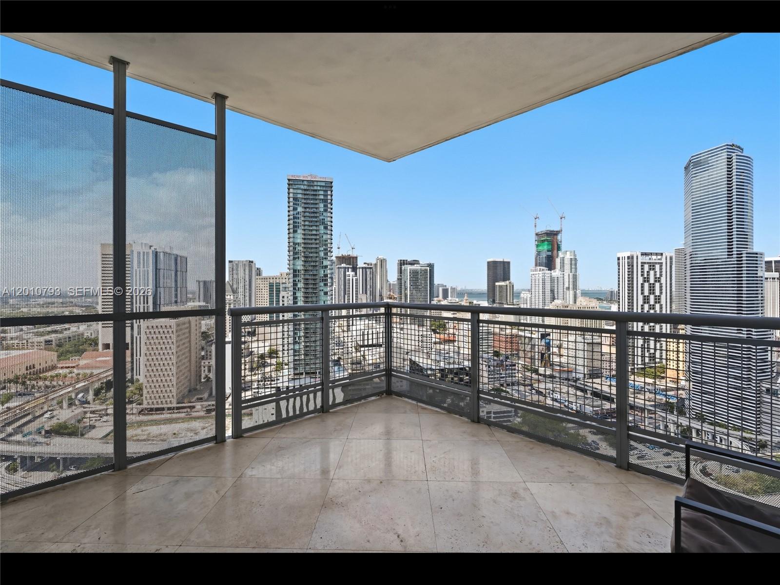 A high-rise balcony with tiled flooring and metal railings overlooking a dense city skyline — 350 S Miami Ave # 3307, Miami FL 33130, MIAMI, FL