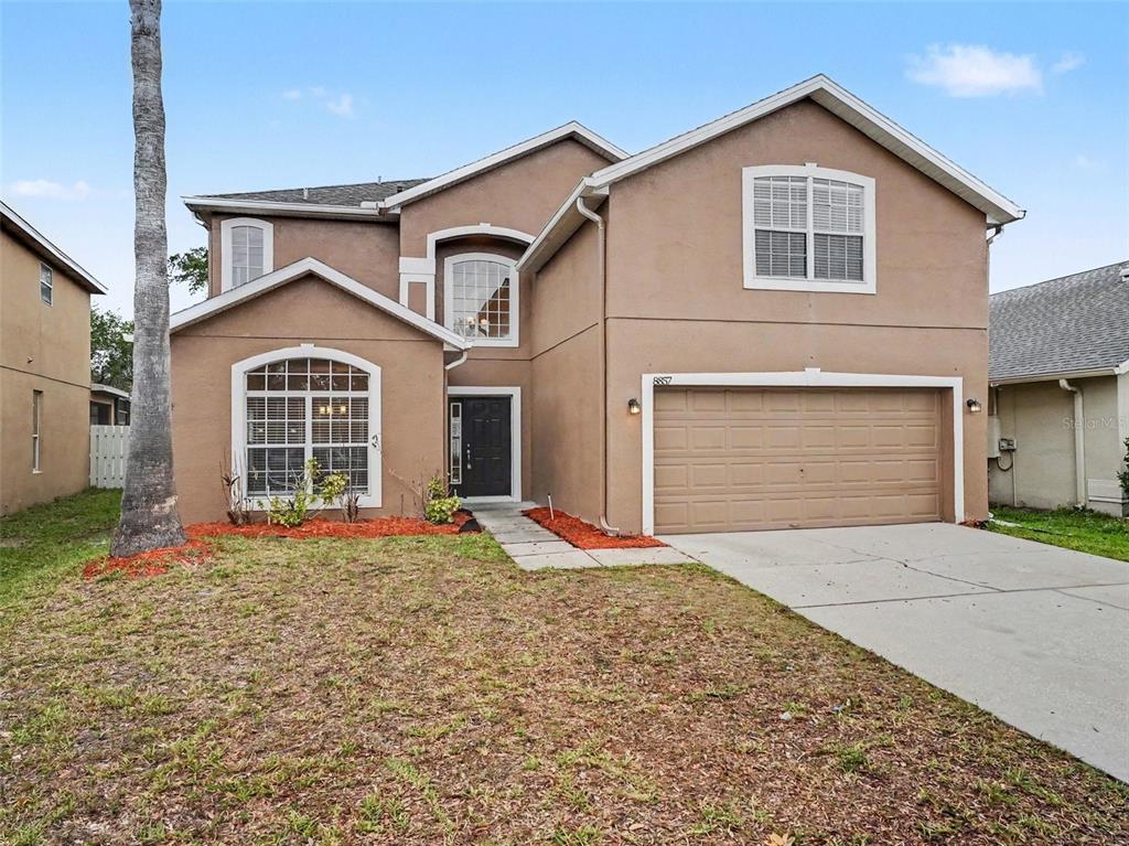A two-story tan stucco house features a front-facing garage and a large arched window — 8857 PALISADES BEACH AVENUE, ORLANDO, FL