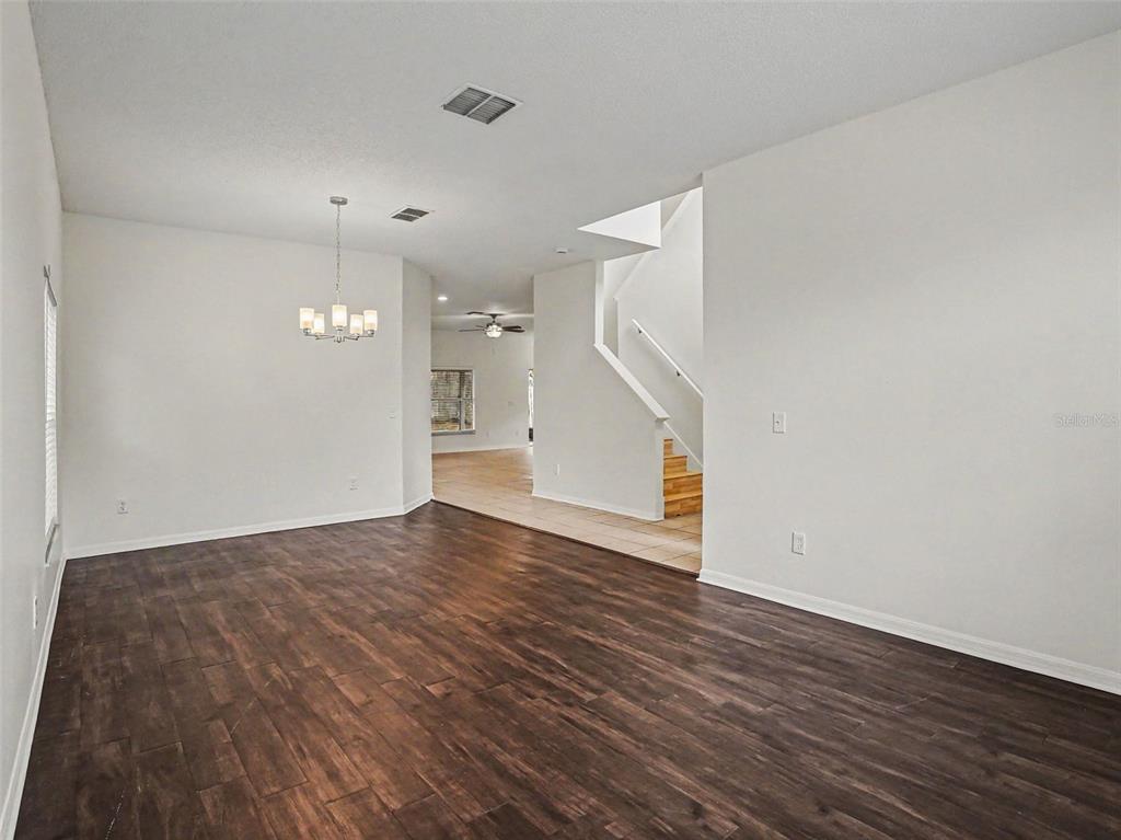 An empty room with dark wood-look flooring, white walls, a chandelier, and a staircase — 8857 PALISADES BEACH AVENUE, ORLANDO, FL