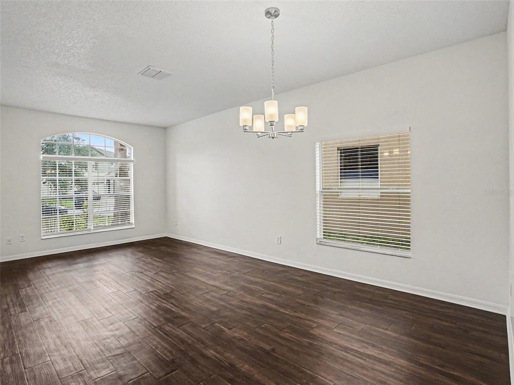 An empty room with dark wood-look flooring, white walls, a chandelier, and two windows — 8857 PALISADES BEACH AVENUE, ORLANDO, FL