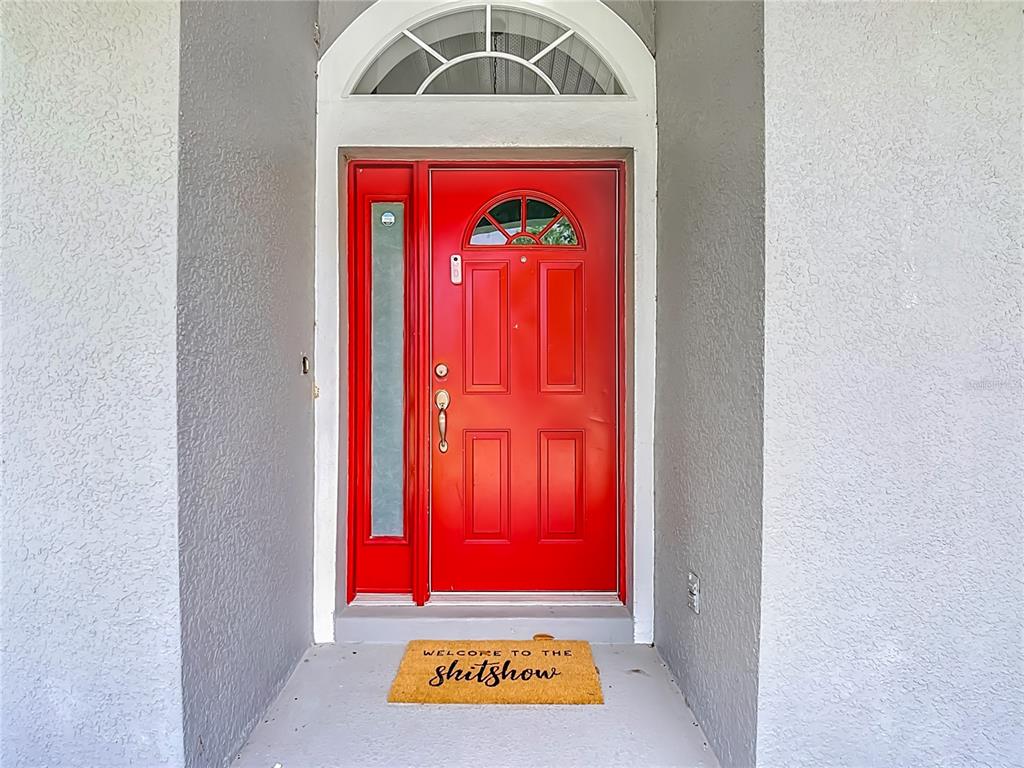 A bright red front door with a sidelight and arched transom sits under a porch — 3600 YELLOW BIRD COURT, ST CLOUD, FL
