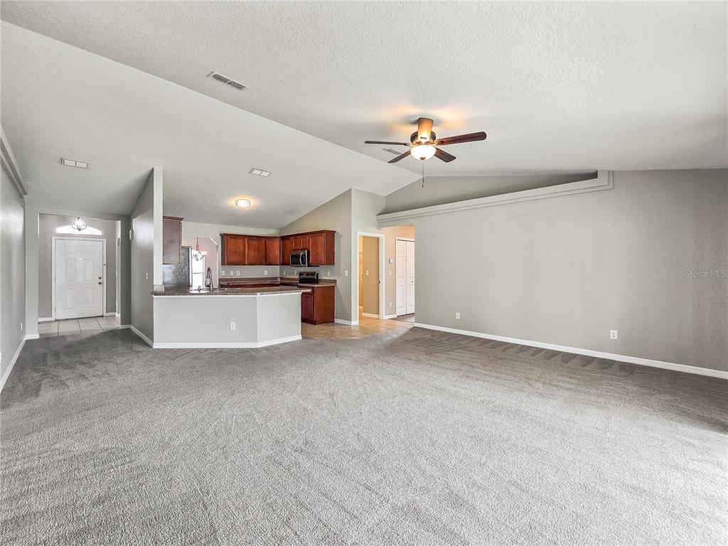 A spacious living room with gray carpet leads to an open kitchen with dark wood cabinets — 37 PECAN RUN PASS, OCALA, FL