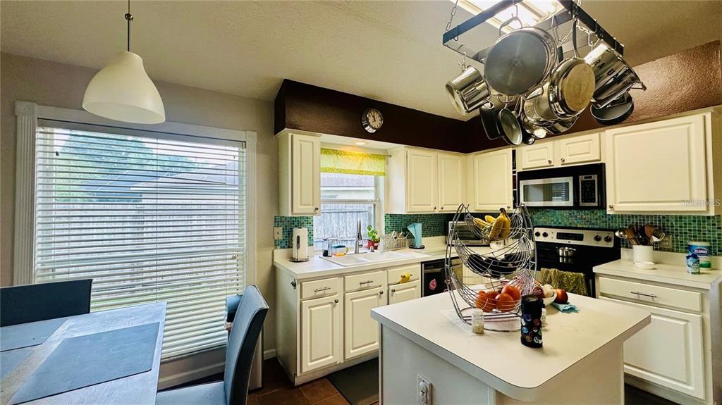 A kitchen with white cabinets, a central island, a hanging pot rack, and a dining area — 3227 HERONS POINT CIRCLE, KISSIMMEE, FL