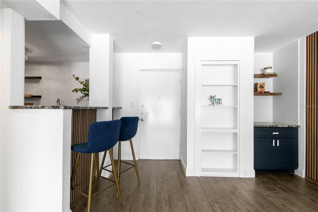 A kitchen area features a breakfast bar with blue stools, white walls, and wood flooring — 2302 S MANHATTAN AVENUE UNIT 108, TAMPA, FL