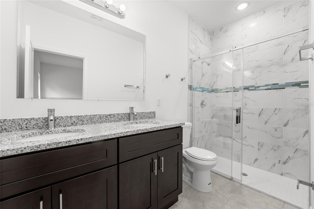 A bathroom with a double vanity, granite countertops, dark cabinets, and a glass-enclosed shower — 3179 W BARBERTON PLACE, CITRUS SPRINGS, FL