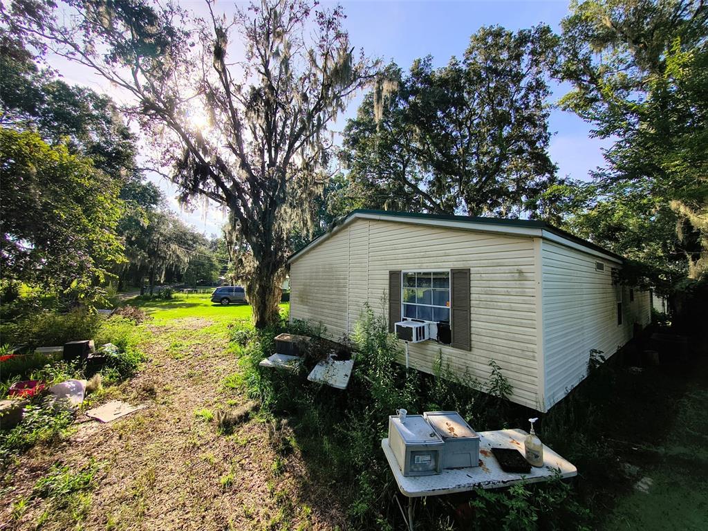 A light-colored mobile home sits on a grassy lot surrounded by trees and overgrown vegetation — 3609 MAXWELL ROAD, PLANT CITY, FL