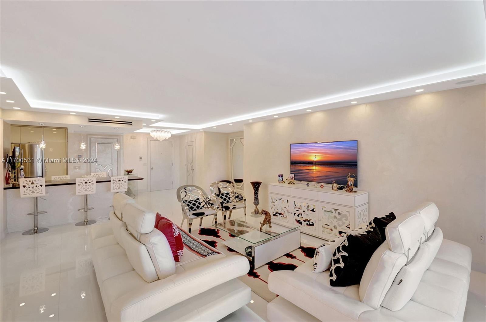 A modern living room features white leather sofas, a glass coffee table, and recessed lighting — 9801 W Collins Ave, Bal Harbour FL 33154, BAL HARBOUR, FL