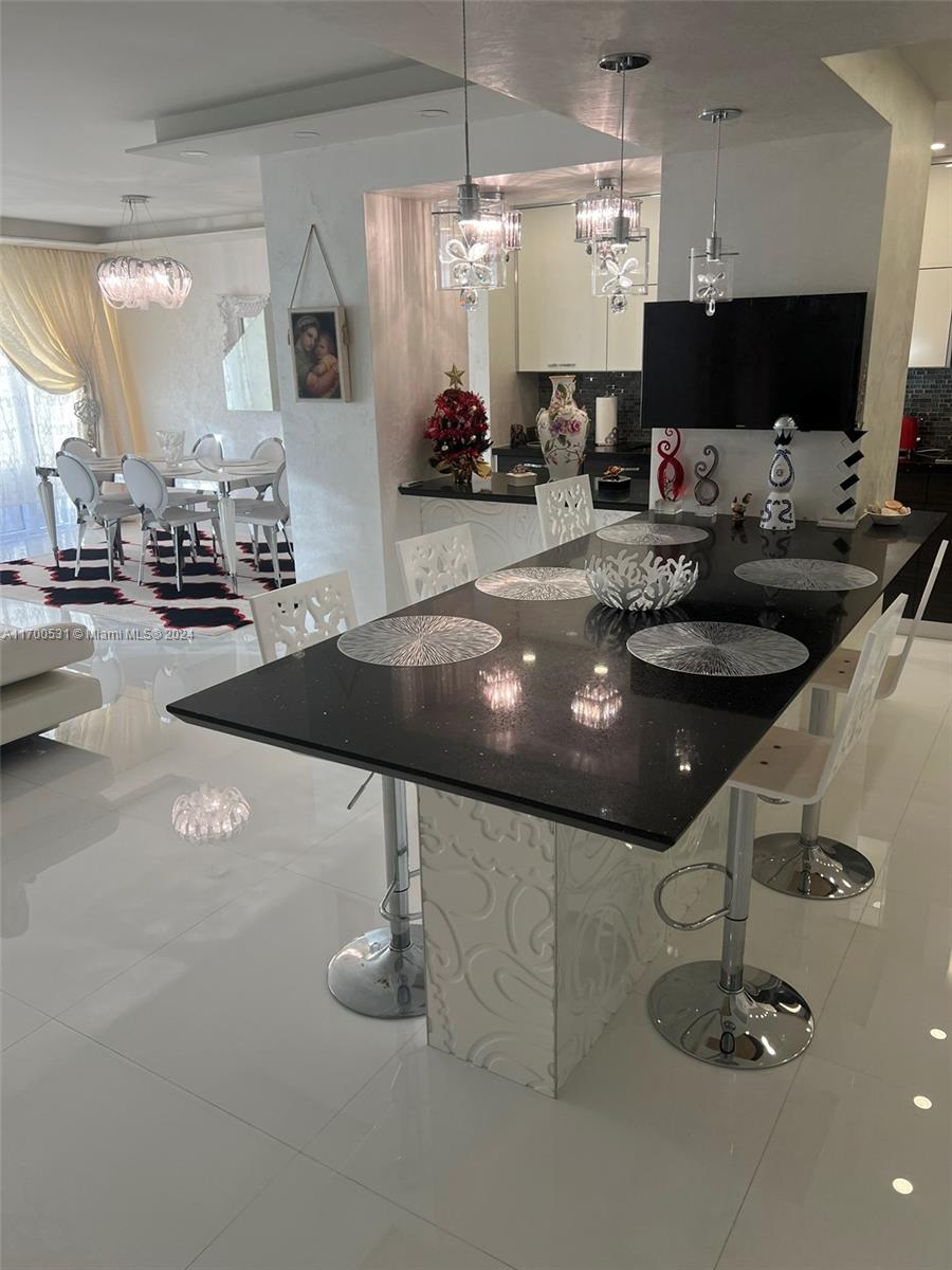 A modern kitchen features a black quartz island with bar stools and white tile flooring — 9801 W Collins Ave, Bal Harbour FL 33154, BAL HARBOUR, FL