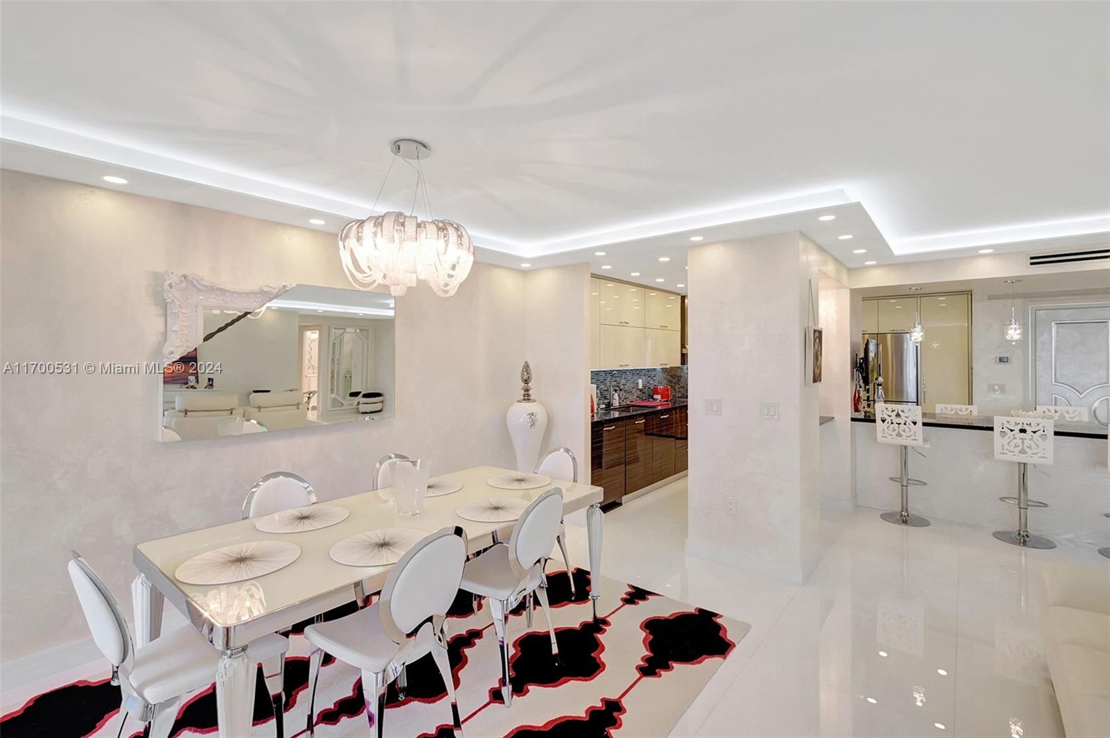A dining area with a modern chandelier, white furniture, and a patterned rug — 9801 W Collins Ave, Bal Harbour FL 33154, BAL HARBOUR, FL