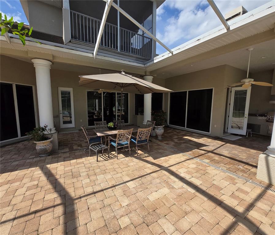 A screened-in patio features a paved floor, outdoor dining set with an umbrella, and columns — 19153 GERACI ROAD, LUTZ, FL