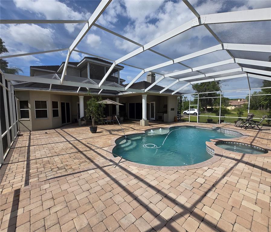 A screened-in patio features a swimming pool, a hot tub, and paver flooring — 19153 GERACI ROAD, LUTZ, FL