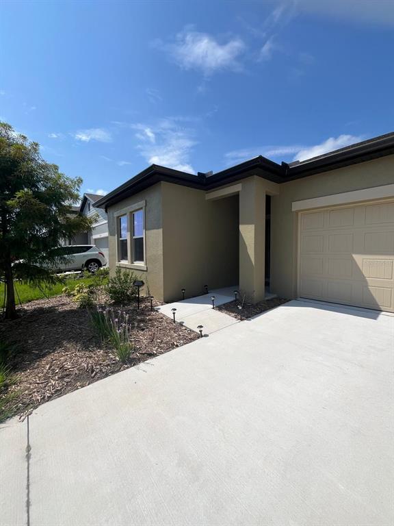 A tan house exterior features a concrete driveway, a garage, and a small landscaped front yard — 1332 DALKEITH COVE, SANFORD, FL