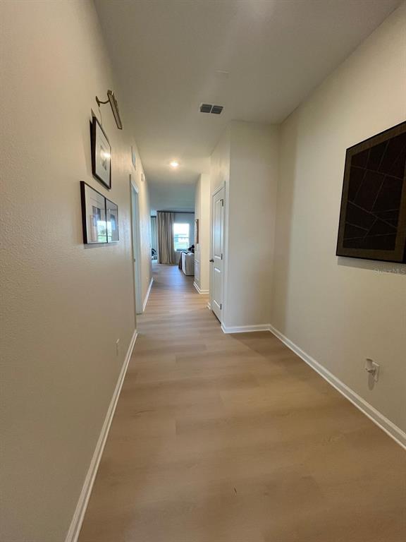 A hallway with light wood-look flooring leads toward a bright living area in the distance — 1332 DALKEITH COVE, SANFORD, FL
