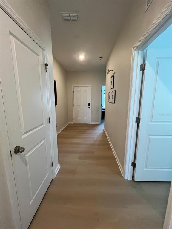 A hallway with light wood-look flooring leads to a white front door — 1332 DALKEITH COVE, SANFORD, FL